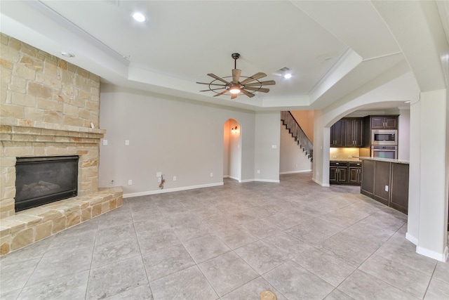 unfurnished living room featuring arched walkways, recessed lighting, a ceiling fan, a fireplace, and a raised ceiling