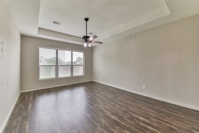 spare room featuring a raised ceiling, visible vents, a ceiling fan, dark wood-type flooring, and baseboards