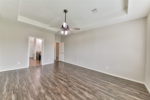 empty room featuring a tray ceiling, baseboards, a ceiling fan, and dark wood-style floors
