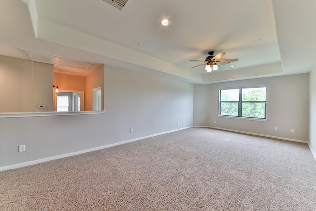 carpeted empty room with attic access, a ceiling fan, baseboards, and a raised ceiling