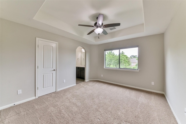 spare room with a tray ceiling, a ceiling fan, arched walkways, baseboards, and light colored carpet