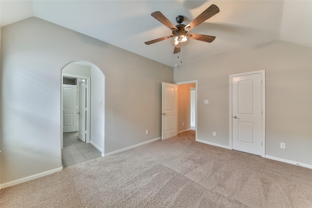 unfurnished bedroom featuring lofted ceiling, baseboards, arched walkways, and light colored carpet