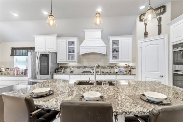 7407 Tudor Heights Ln, Spring, TX 77379 - kitchen featuring stainless steel appliances, custom exhaust hood, decorative backsplash, white cabinetry, and vaulted ceiling
