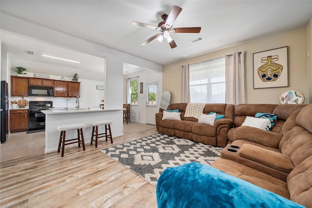 living room with a ceiling fan, visible vents, and light wood-style flooring