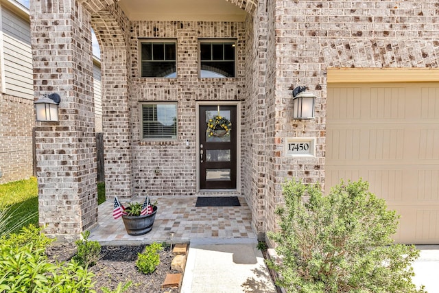 entrance to property featuring a garage and brick siding