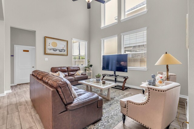 living area featuring a high ceiling, a ceiling fan, wood finished floors, and baseboards