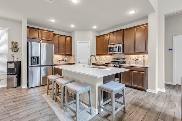 kitchen featuring a sink, stainless steel appliances, a kitchen bar, baseboards, and wood finish floors