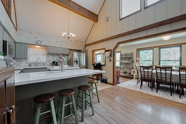 kitchen featuring an inviting chandelier, gray cabinets, a breakfast bar, high vaulted ceiling, and appliances with stainless steel finishes