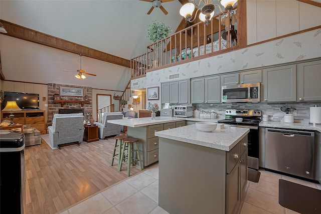 kitchen with gray cabinets, high vaulted ceiling, stainless steel appliances, and ceiling fan with notable chandelier