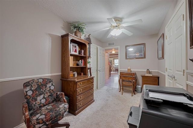 home office with a textured ceiling, visible vents, a ceiling fan, and light colored carpet