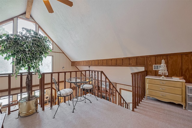 living area with a ceiling fan, an upstairs landing, lofted ceiling with beams, carpet, and wood walls
