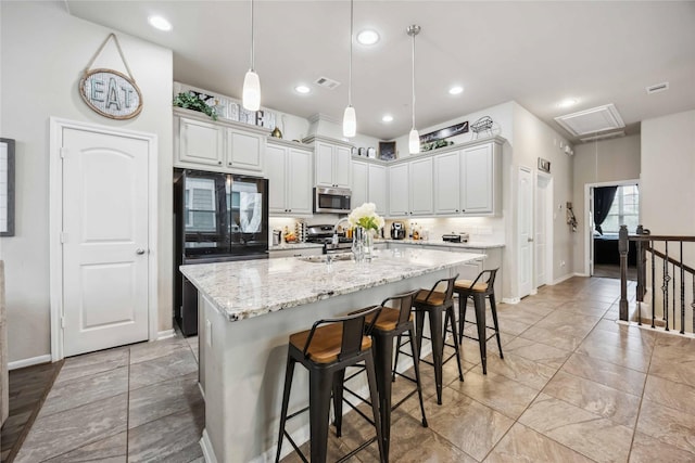 kitchen with stainless steel microwave, visible vents, a kitchen bar, light stone countertops, and an island with sink