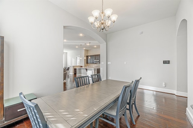 dining space featuring arched walkways, an inviting chandelier, baseboards, dark wood-style flooring, and recessed lighting