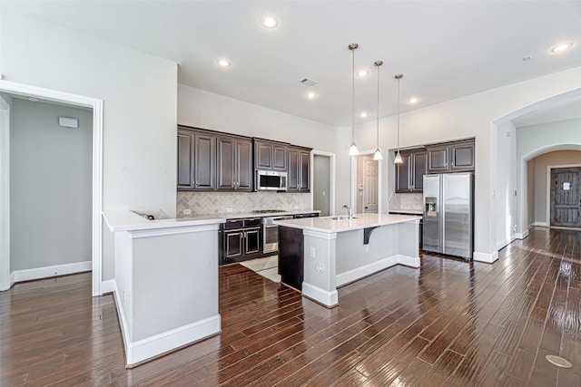 kitchen featuring a breakfast bar, light countertops, a sink, arched walkways, and appliances with stainless steel finishes