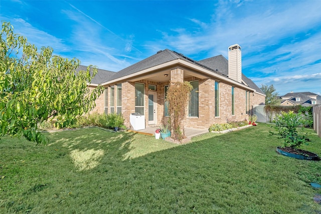 back of house featuring a chimney, fence, brick siding, a lawn, and a patio