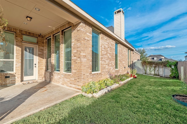 view of side of property with a chimney, fence, brick siding, a patio area, and a lawn