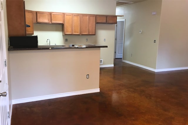 kitchen with concrete flooring, dark countertops, baseboards, and brown cabinets