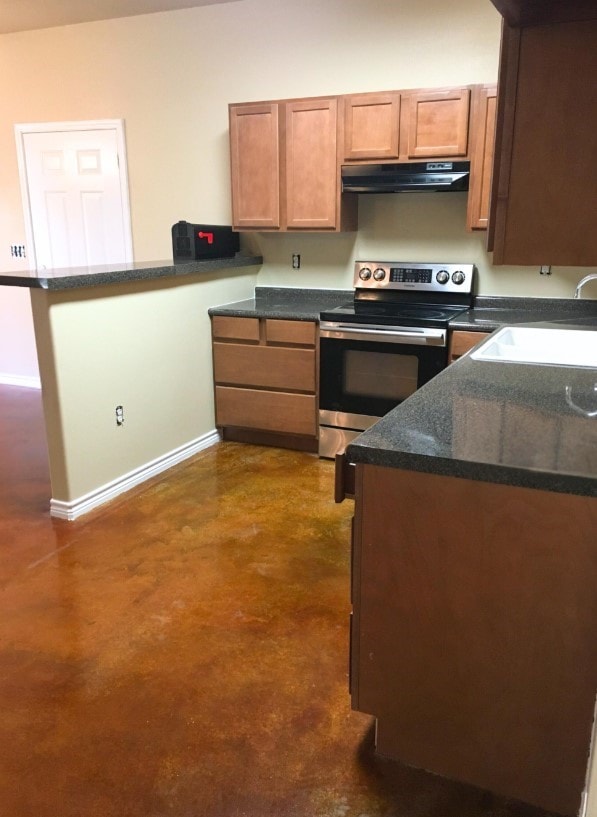 kitchen with a sink, concrete flooring, stainless steel electric range oven, a peninsula, and under cabinet range hood