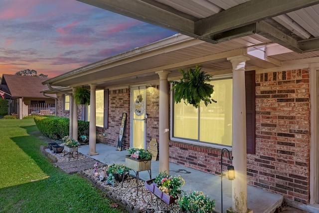 exterior entry at dusk featuring brick siding, a lawn, and a porch