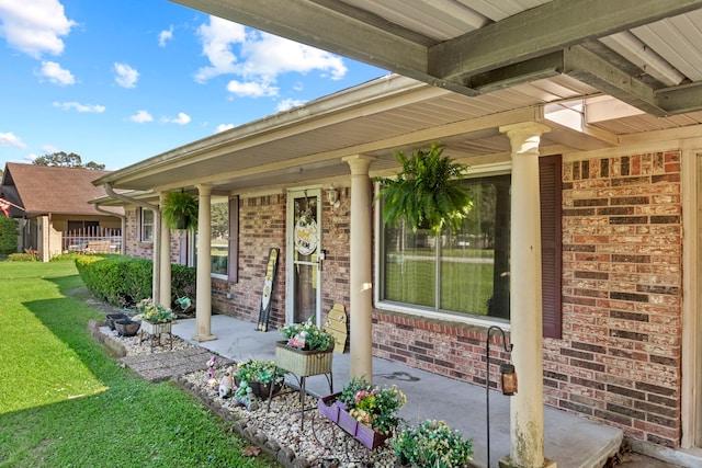 entrance to property featuring covered porch, brick siding, and a yard