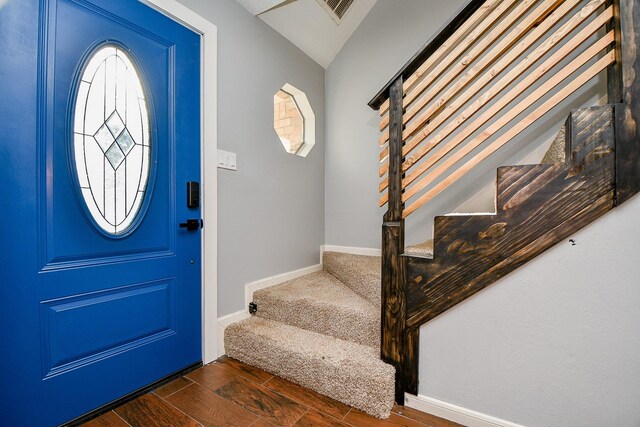 foyer entrance featuring dark wood-style flooring, vaulted ceiling, visible vents, baseboards, and stairs