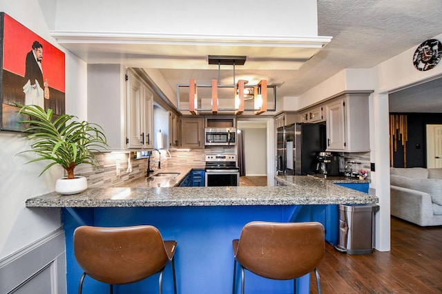 kitchen with stainless steel appliances, a peninsula, a sink, dark wood-style flooring, and decorative backsplash