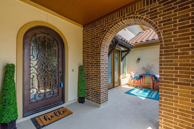 property entrance with brick siding, a tile roof, and stucco siding