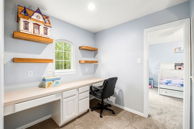 office space with built in study area, baseboards, and light carpet