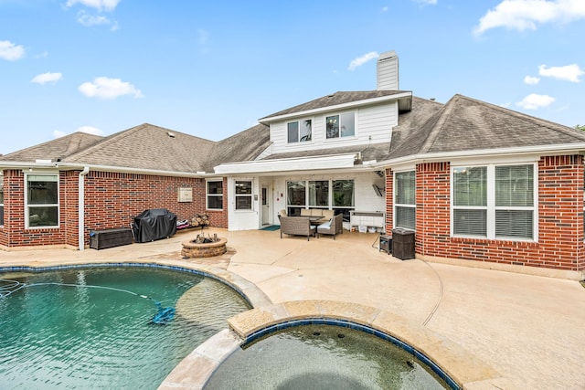 back of house featuring an in ground hot tub, a chimney, a patio area, and brick siding