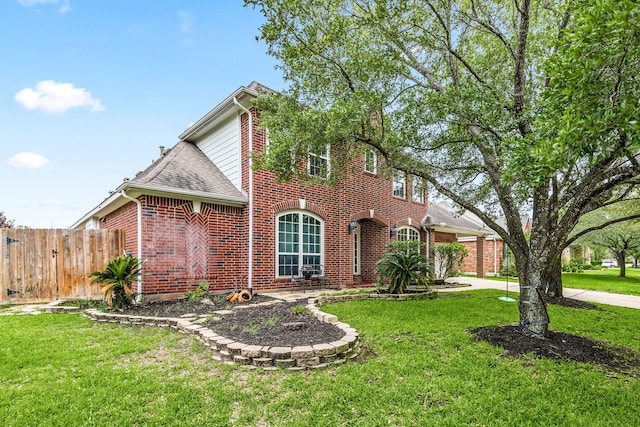 view of front of house with brick siding, fence, a shingled roof, and a front lawn