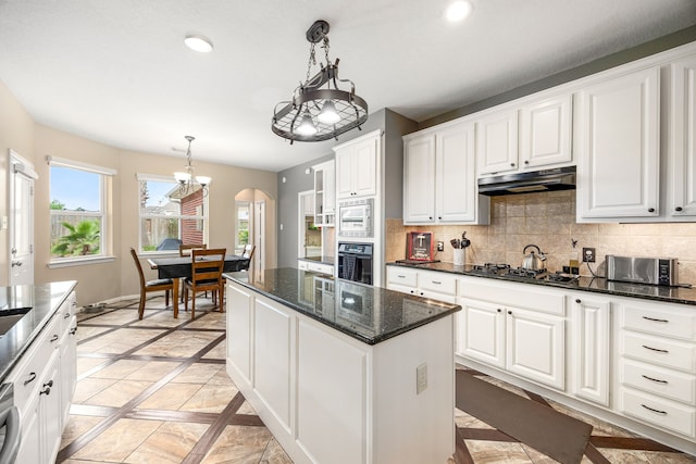 kitchen featuring decorative backsplash, black oven, white cabinetry, stainless steel microwave, and under cabinet range hood