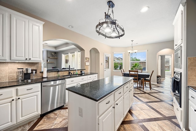 kitchen featuring an inviting chandelier, a kitchen island, white cabinets, arched walkways, and appliances with stainless steel finishes