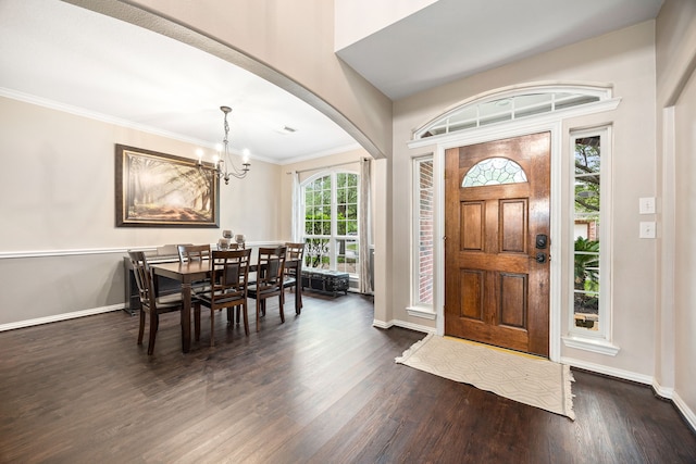 entrance foyer featuring ornamental molding, baseboards, dark wood-type flooring, arched walkways, and a notable chandelier