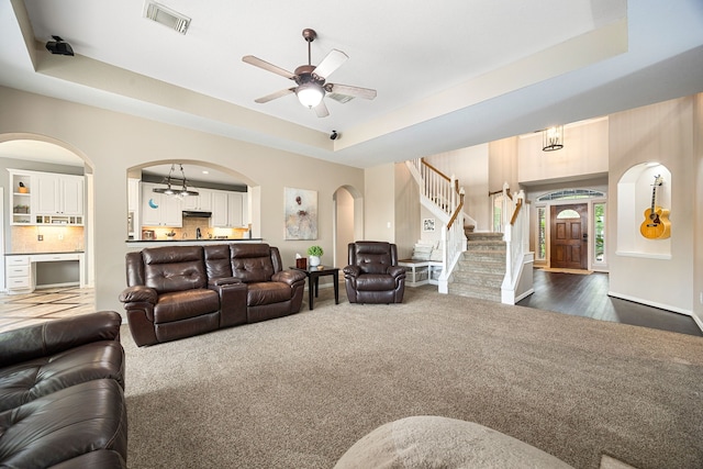 living area with visible vents, stairs, dark carpet, a raised ceiling, and arched walkways