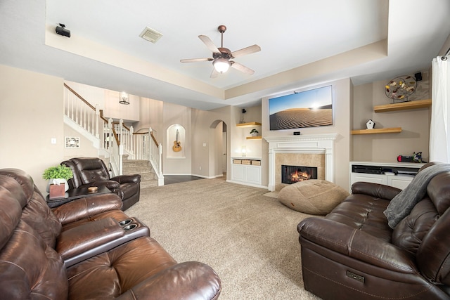 living area with carpet flooring, ceiling fan, arched walkways, a tray ceiling, and visible vents