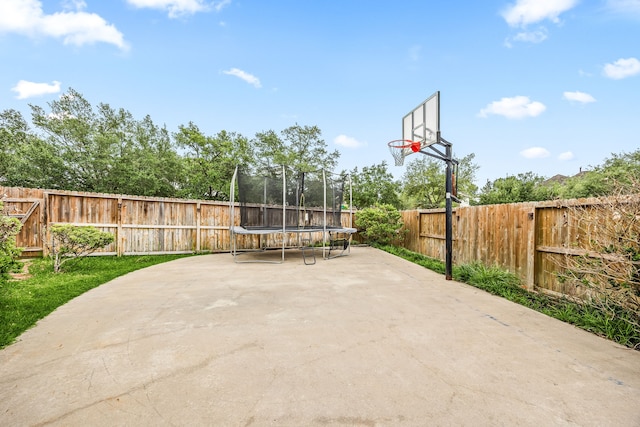 view of sport court with a fenced backyard and a trampoline