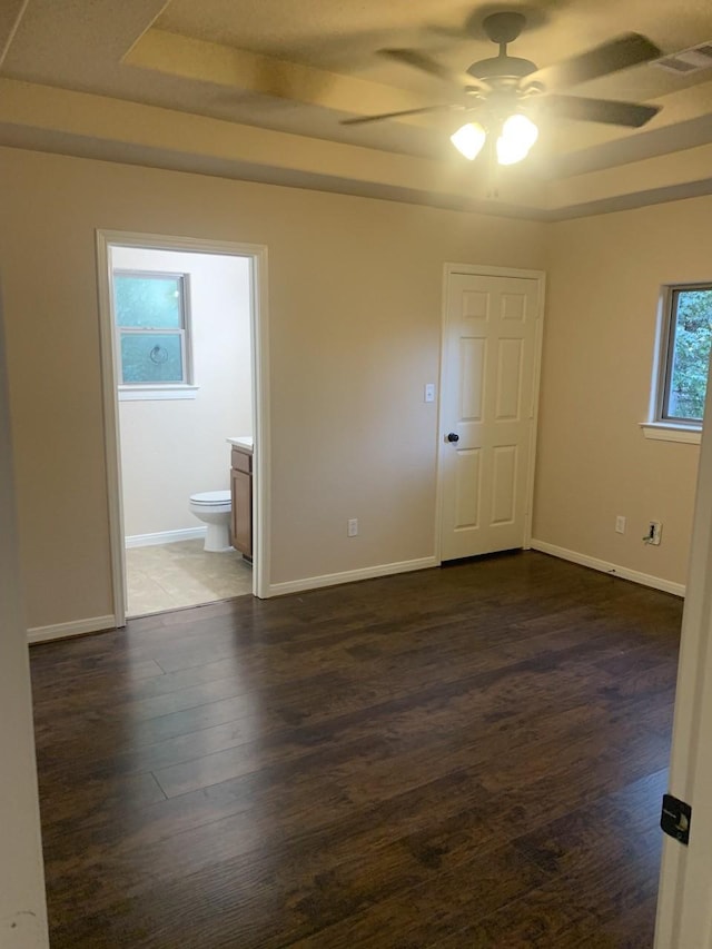 spare room with ceiling fan, a tray ceiling, visible vents, baseboards, and dark wood-style flooring