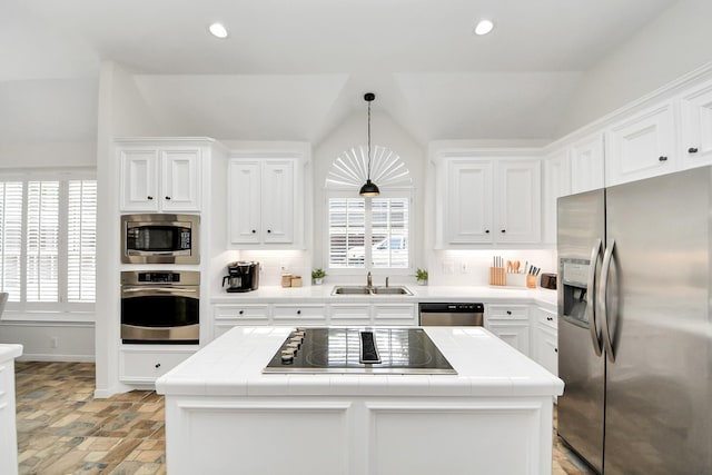 kitchen featuring tile counters, appliances with stainless steel finishes, a sink, and lofted ceiling