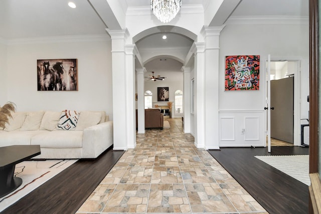 hallway featuring crown molding, arched walkways, baseboards, stone tile flooring, and ornate columns