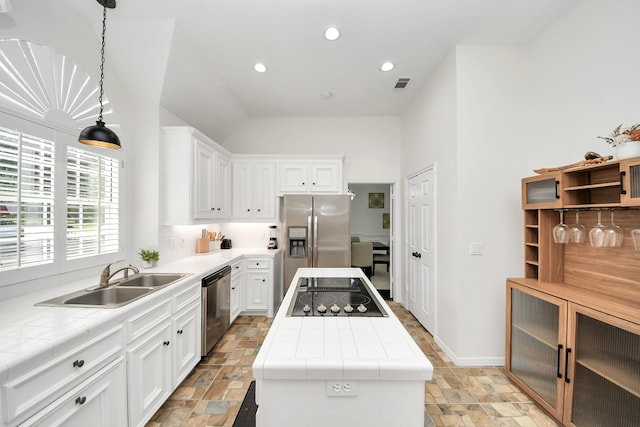kitchen with appliances with stainless steel finishes, a center island, a sink, stone tile flooring, and tile counters