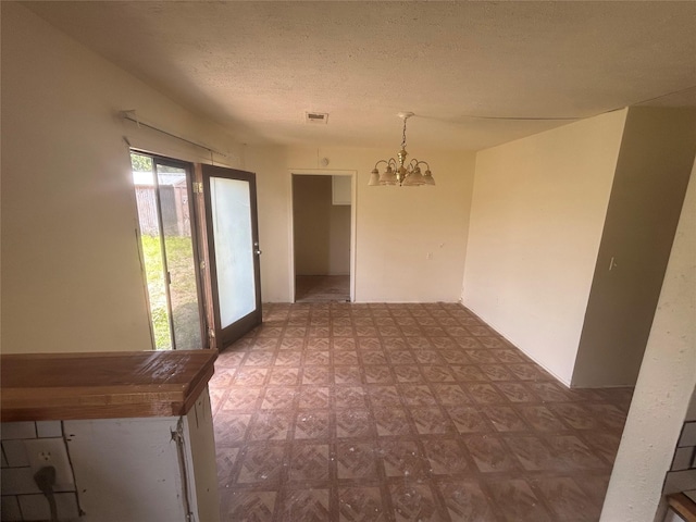 unfurnished dining area with a textured ceiling, visible vents, tile patterned floors, and a notable chandelier
