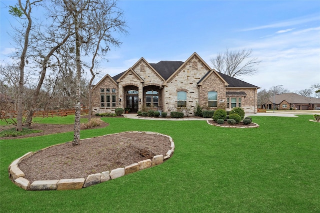 french country home featuring stone siding, french doors, brick siding, and a front yard