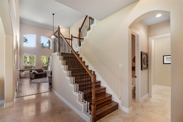 stairs with baseboards, a high ceiling, arched walkways, and tile patterned floors