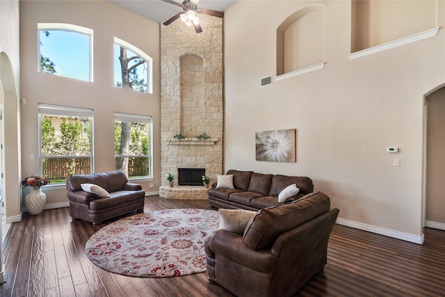living area with arched walkways, visible vents, a towering ceiling, ceiling fan, and a fireplace