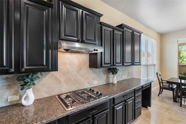 kitchen with stainless steel gas stovetop, under cabinet range hood, dark cabinetry, baseboards, and decorative backsplash