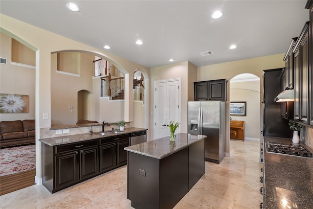 kitchen featuring a sink, arched walkways, dark stone counters, a kitchen island, and appliances with stainless steel finishes