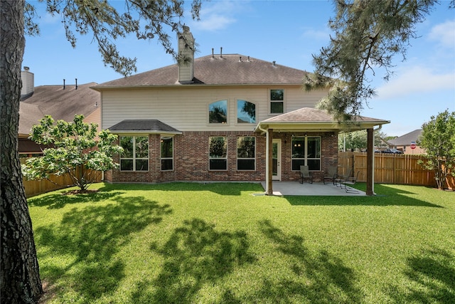 back of property featuring a chimney, a lawn, a fenced backyard, a patio, and brick siding