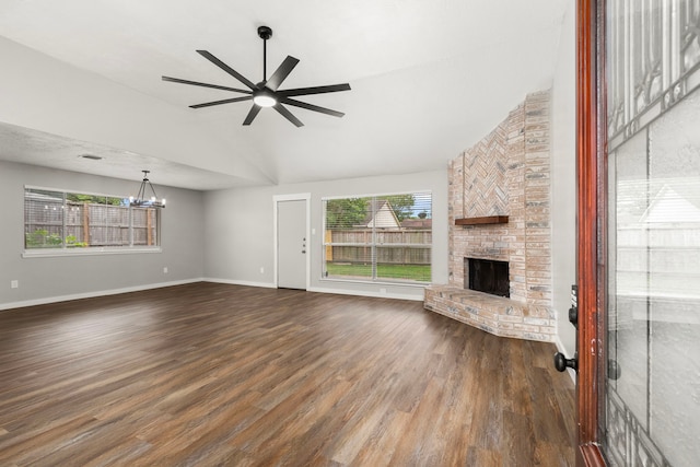 unfurnished living room with a brick fireplace, baseboards, high vaulted ceiling, dark wood-type flooring, and ceiling fan with notable chandelier