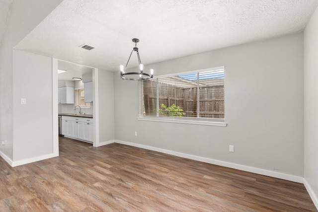 unfurnished dining area with wood finished floors, baseboards, a chandelier, and visible vents