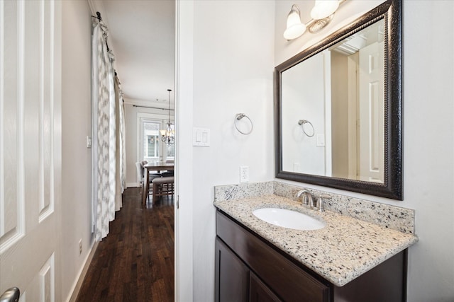 bathroom with vanity, a chandelier, wood finished floors, and baseboards